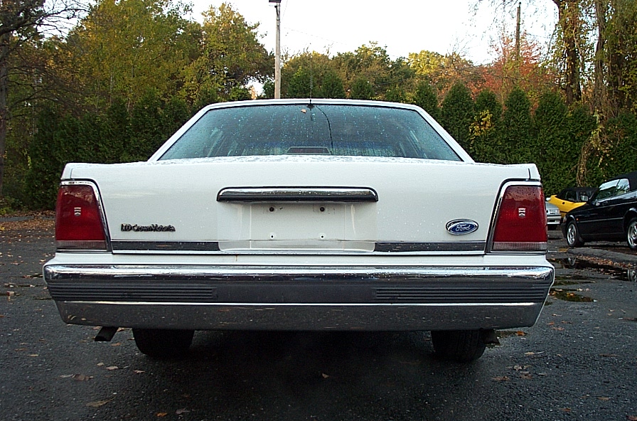 Rear view of a white 1991 Ford Crown Victoria LTD. Another car is parked to the right