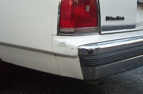 1991 Ford LTD Crown Victoria - The rear of a white 1991 Ford Crown Victoria LTD shows a damaged bumper and chrome accents.