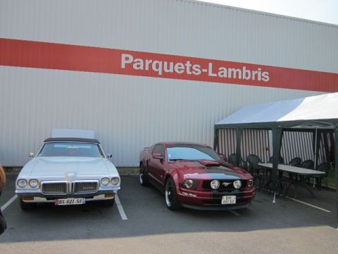 1991 Ford LTD Crown Victoria - Two cars are parked in front of a building with a red stripe and text. A tent is set up to the right.