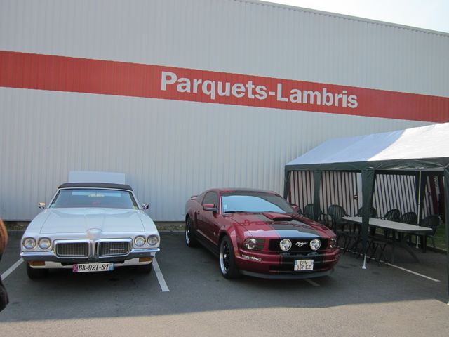 White convertible and red Ford Mustang parked outside a building with 'Parquets-Lambris' sign