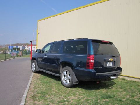 1991 Ford LTD Crown Victoria - A dark blue Chevrolet Suburban is parked on a grassy area next to a building with a yellow trim.