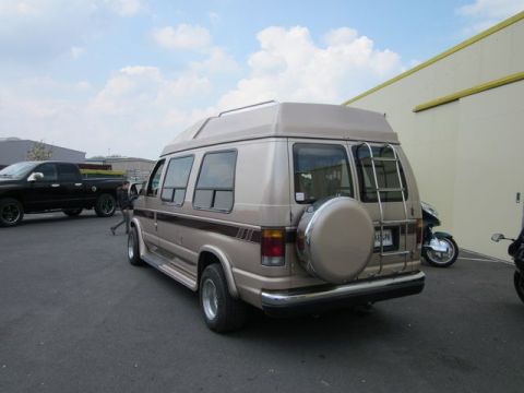 1991 Ford LTD Crown Victoria - Rear view of a tan Ford Econoline van parked next to a black pickup truck and a motorcycle.