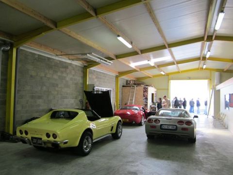 1991 Ford LTD Crown Victoria - Three Chevrolet Corvettes are parked inside a garage, one with its hood open.