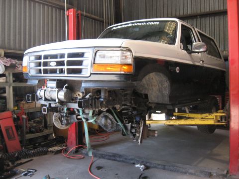 1994 Ford Bronco - A two-tone Ford Bronco is undergoing front-end repairs on a hydraulic lift in a garage.