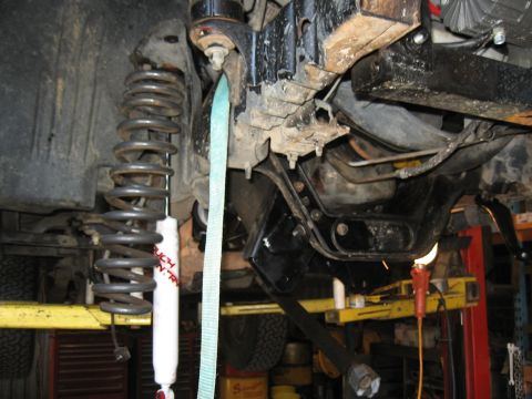 1994 Ford Bronco - The underside of a vehicle is shown with its suspension components, including a shock and coil spring, secured by a strap.