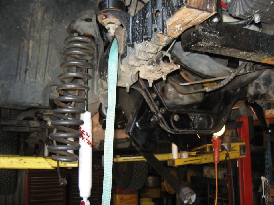 close-up of vehicle suspension with shock absorber and coil spring, held by a strap