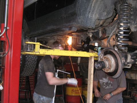 1994 Ford Bronco - Two mechanics are seen working on the underside of a vehicle that is elevated on a lift in a garage.
