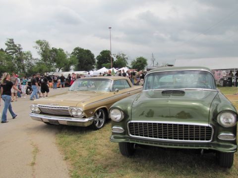 2006 BMW 5 Series - Two vintage cars are displayed at an outdoor event with spectators milling around.