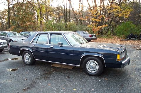 1991 Ford LTD Crown Victoria - This 1991 Ford Crown Victoria LTD is parked outside in an area with other vehicles and trees.