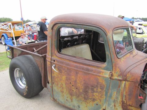 2006 BMW 5 Series - A heavily rusted pickup truck with drag racing tires is displayed at an outdoor car show.