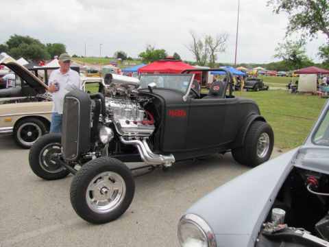 2006 BMW 5 Series - A custom black hot rod with a prominent V8 engine is displayed at an outdoor car show.