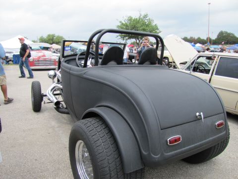 2006 BMW 5 Series - A matte black hot rod roadster is parked at an outdoor event with other vehicles and tents in the background.