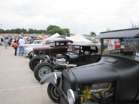 2006 BMW 5 Series - A collection of classic hot rod cars are displayed at an outdoor gathering, with spectators in the background.