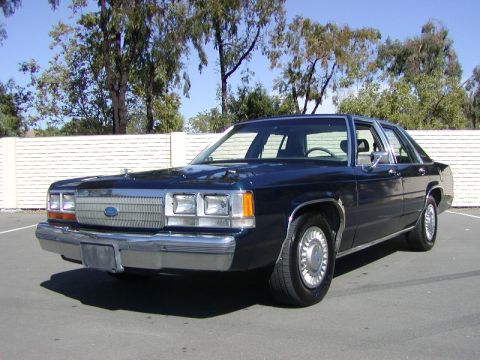 1991 Ford LTD Crown Victoria - Dark blue Ford Crown Victoria four-door sedan photographed from the 3/4 front left in a sunny parking lot beside a white block wall and euc…