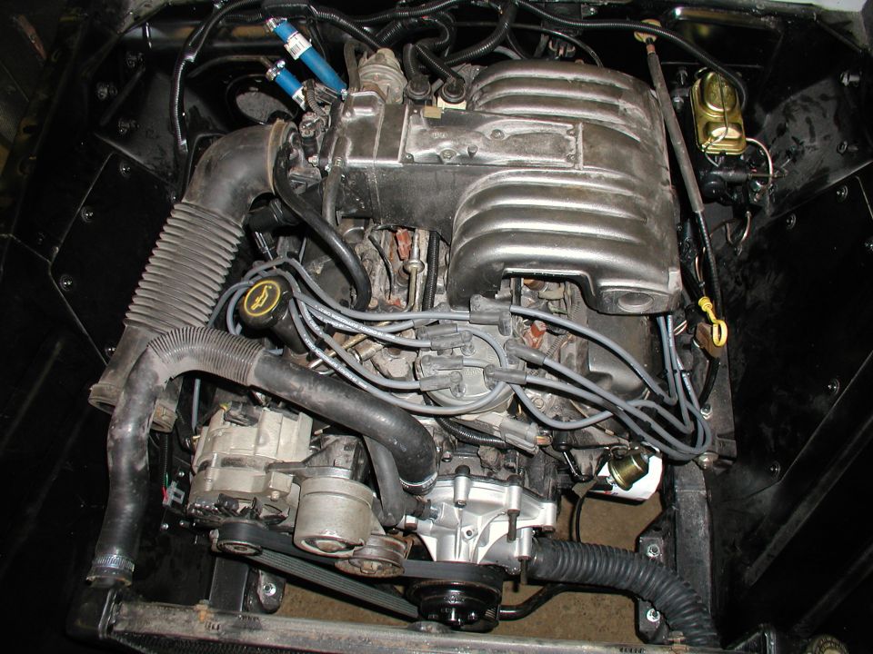 Engine bay with V8 engine, intake manifold, distributor, alternator, and hoses visible. Supermotors.net logo in corner