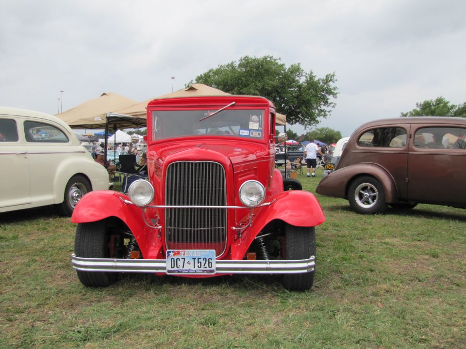 Red hot rod truck with a Texas license plate DC7-T526, parked on grass with other vintage cars and tents in the background