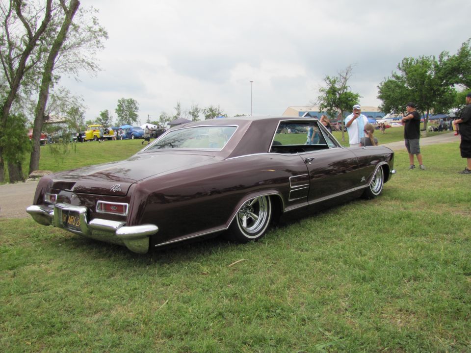 Maroon 1966 Buick Riviera with chrome accents and whitewall tires, parked on grass