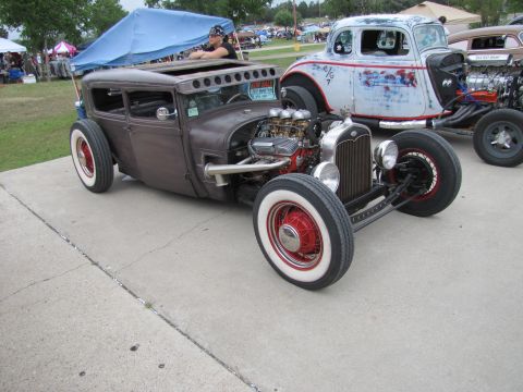 2006 BMW 5 Series - A custom hot rod with a prominent engine and whitewall tires is parked next to another vehicle at an outdoor event.