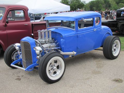 2006 BMW 5 Series - A custom blue hot rod coupe is parked next to a maroon pickup truck at an outdoor event.