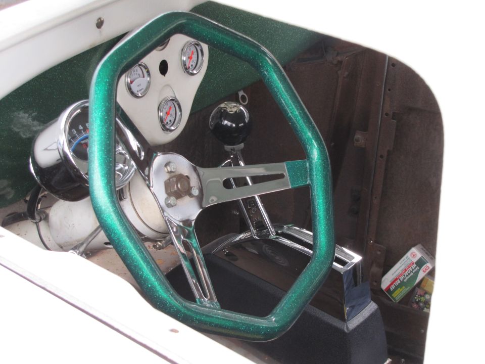 Custom green steering wheel, dashboard with gauges, and a black shift knob in a hot rod