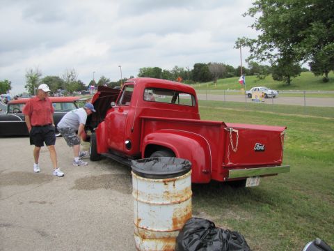 2006 BMW 5 Series - Red 1953 Ford F-series pickup truck at an outdoor event with two people inspecting the engine.