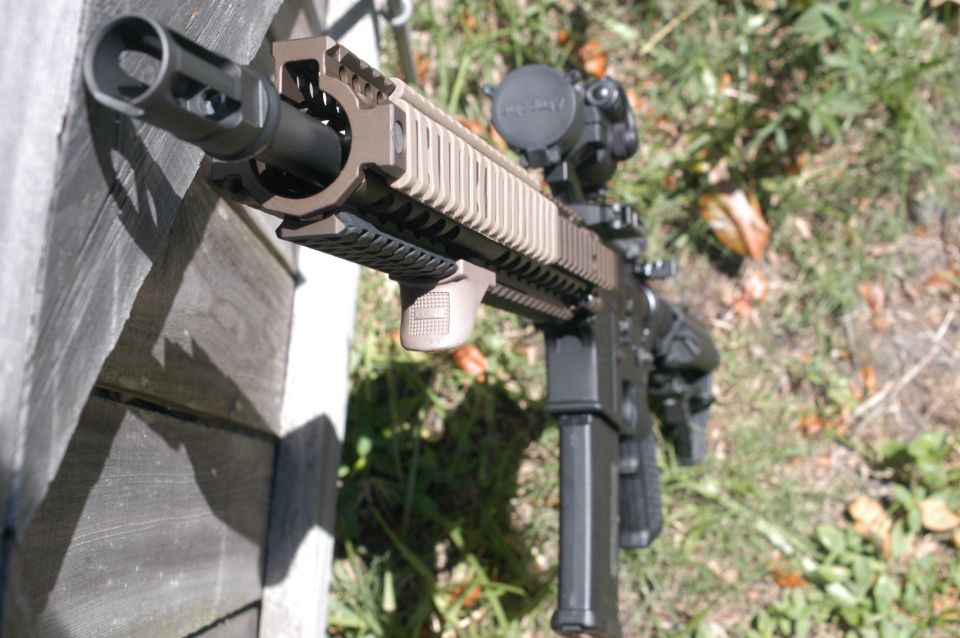 Close-up of an assault rifle with a scope, resting against a wooden surface outdoors
