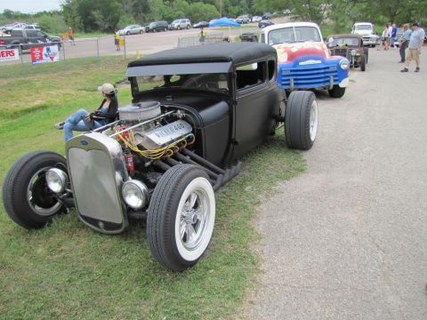 2006 BMW 5 Series - A custom hot rod is parked next to a classic blue and red truck at an outdoor event.