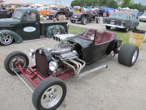 2006 BMW 5 Series - A custom hot rod with a prominent supercharger and side exhaust pipes is displayed at an outdoor car show.