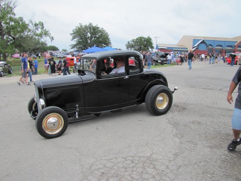 2006 BMW 5 Series - A black 1932 Ford hot rod coupe is parked at an outdoor car show with people in the background.