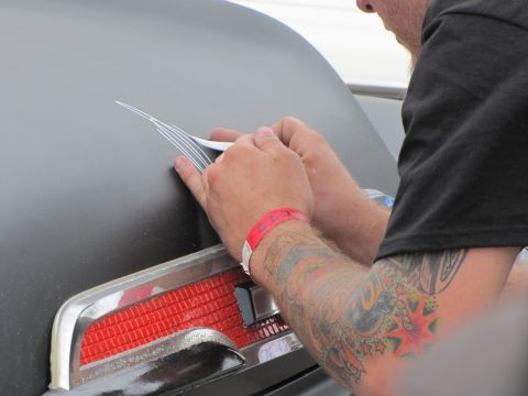 2006 BMW 5 Series - A pinstriper adds detail to a vehicle's trunk, focusing on the area near the red taillight assembly.