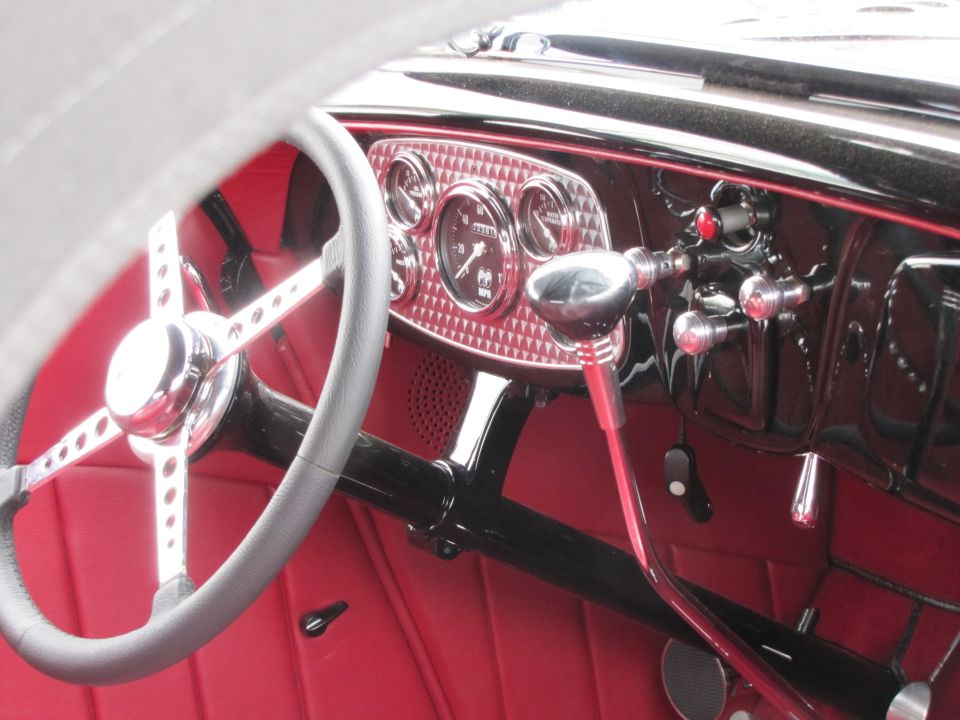 Interior of a hot rod with red seats, a chrome steering wheel, and a diamond-patterned dashboard with gauges