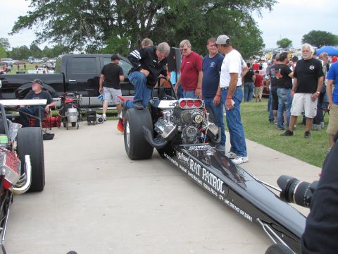 2006 BMW 5 Series - A dragster with 'Rat Patrol' text and a prominent front engine is examined by a group of people at an outdoor event.