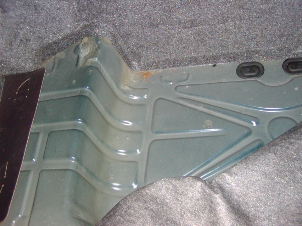 Car trunk floor pan with ribbed metal structure and gray carpet trim