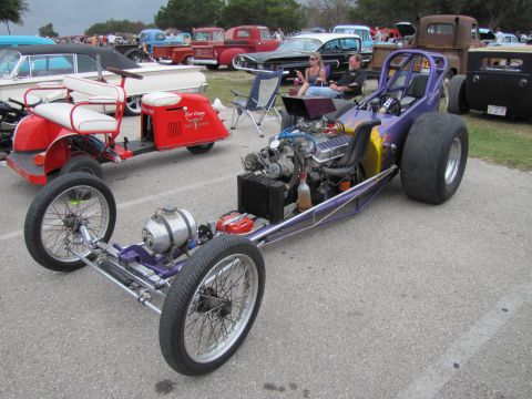 2006 BMW 5 Series - A dragster is parked at an outdoor event with other vehicles and people in the background.