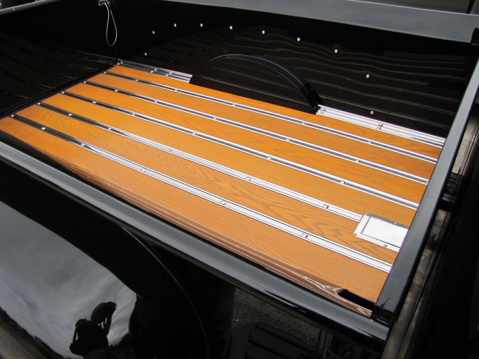 Pickup truck bed with polished wood planks and metal strips. Black sides and wheel well visible