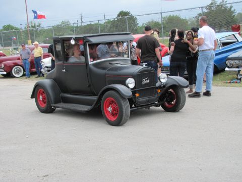 2006 BMW 5 Series - A matte black Ford Model T coupe with bright red wheels is displayed at an outdoor event.
