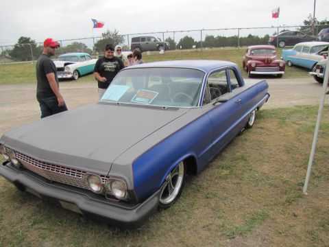 2006 BMW 5 Series - A classic Chevrolet Impala sits on display at an outdoor car show, with other vehicles and attendees visible.
