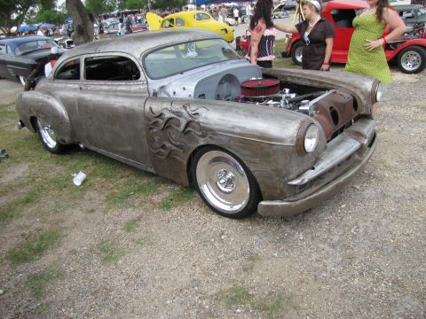 2006 BMW 5 Series - A custom hot rod with a bare metal finish and flame accents on the fender is displayed at an outdoor event.