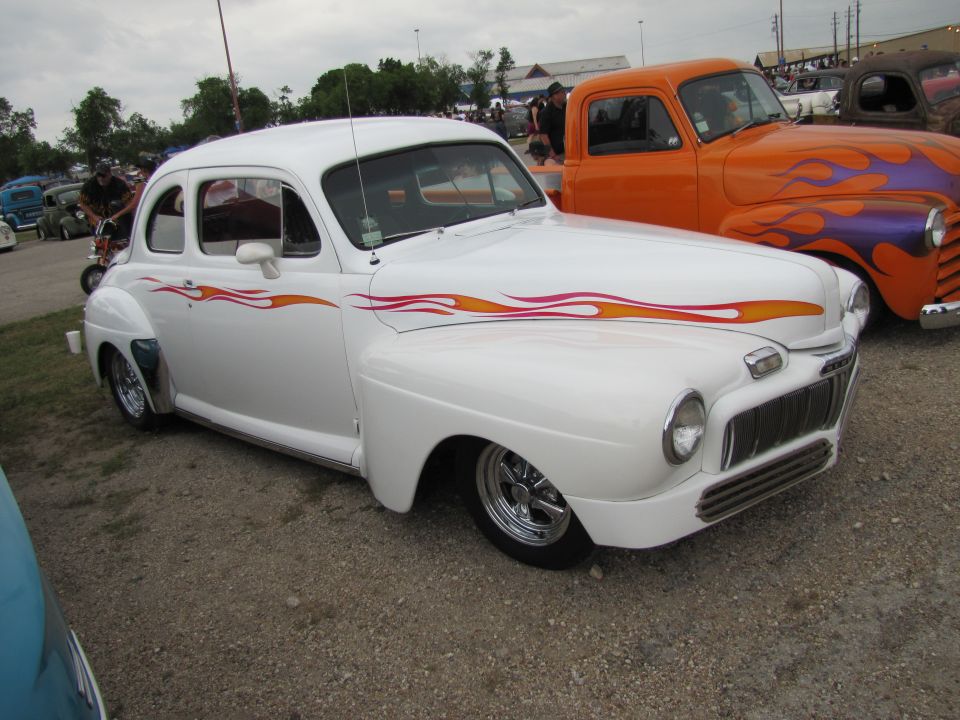 White hot rod with red and yellow flame decals on the side, chrome wheels, and a lowered stance