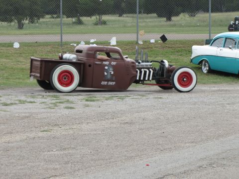 2006 BMW 5 Series - A custom rat rod pickup truck with a unique paint job and exposed engine sits on a dirt lot next to another classic car.
