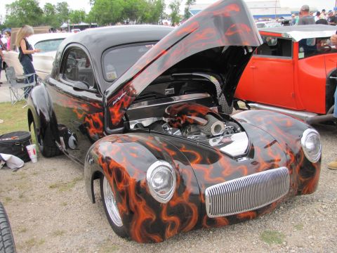 2006 BMW 5 Series - A custom hot rod with a flame paint job is displayed with its hood open, revealing the engine. Another vehicle is visible to the right.