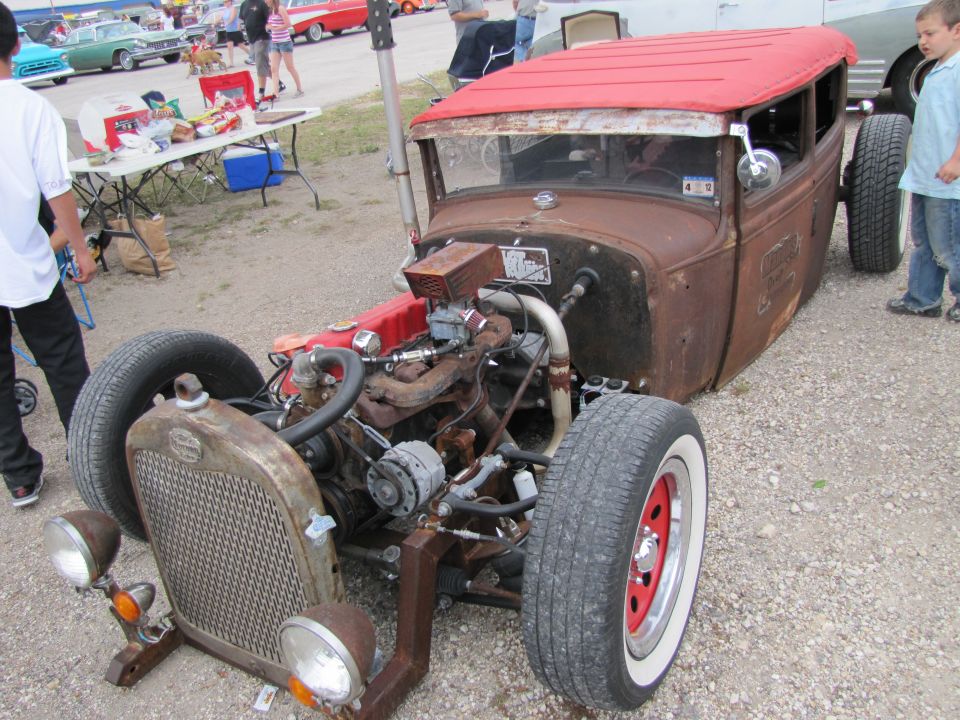 Rusty hot rod with red roof, exposed engine, and whitewall tires