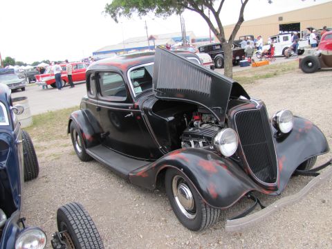 2006 BMW 5 Series - A black hot rod coupe with its hood open is displayed at an outdoor car show, with other vehicles visible in the background.