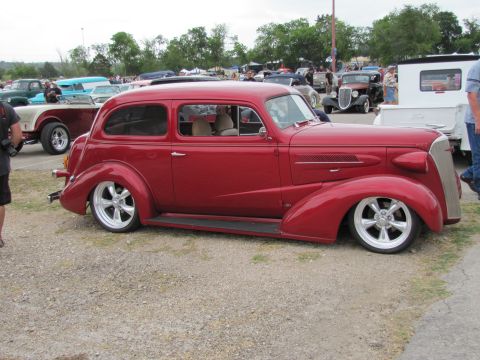 2006 BMW 5 Series - Custom red hot rod sedan with chrome wheels at a car show event.