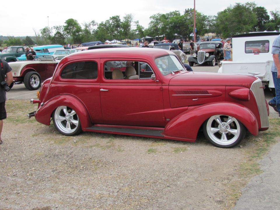 Red hot rod sedan with custom wheels parked at an outdoor car show