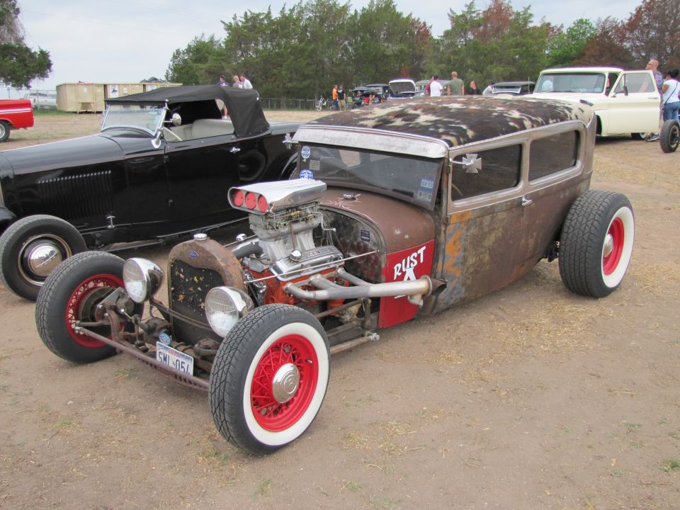 Rusty hot rod sedan with a supercharger, red wire wheels, and white wall tires