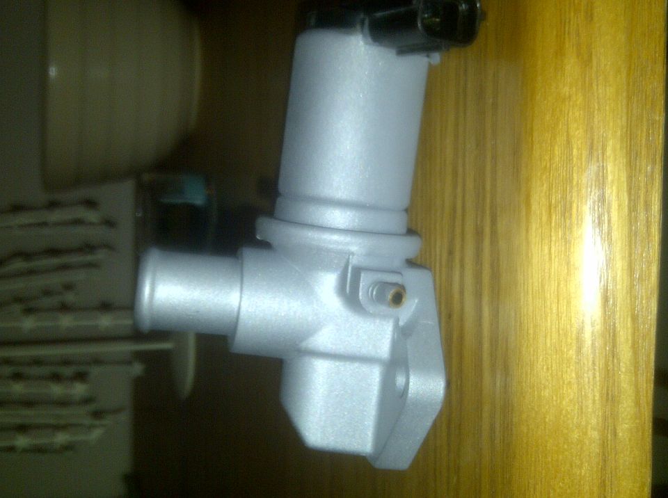Close-up of a silver EGR valve with a black connector on top, mounted against a wood-grain surface