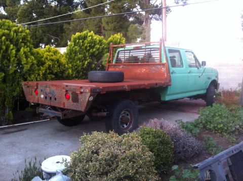 1989 Ford Bronco - A green flatbed truck with a rusty bed and dual rear wheels is parked outdoors.