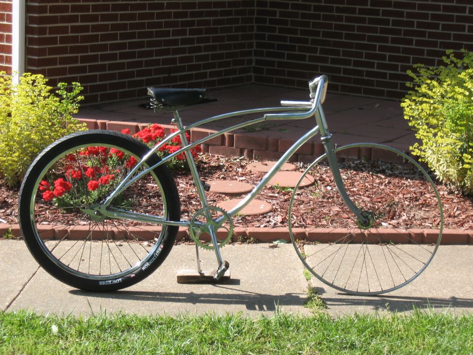 Chrome cruiser bicycle with black seat and red flowers behind the rear wheel