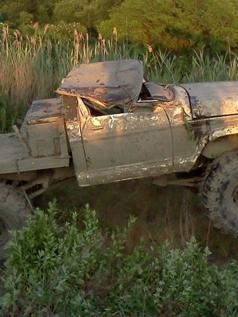 1990 Ford Bronco - This heavily damaged pickup truck appears to be stuck in a muddy, overgrown area.